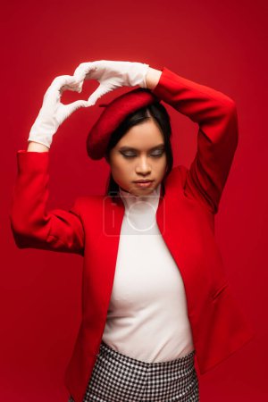 Photo for Fashionable asian model in gloves showing heart sign isolated on red - Royalty Free Image