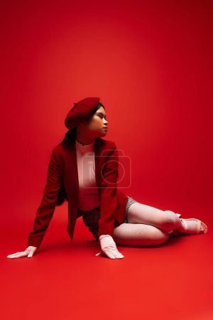 Pretty young asian model in stylish outfit sitting on red background 