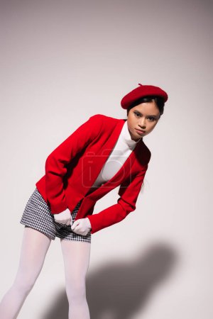 Pretty asian model in red jacket and plaid shorts posing on grey background 