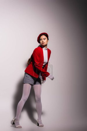 Foto de Brunette asian model in stylish red and white outfit looking away on grey background with shadow - Imagen libre de derechos