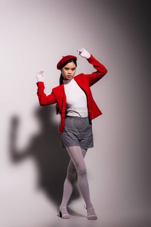 Fashionable asian model in red and white clothes looking at camera on grey background 