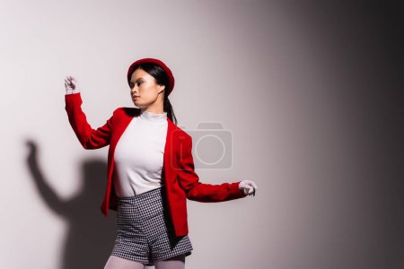 Asian model in gloves and plaid shorts posing on grey background with shadow 