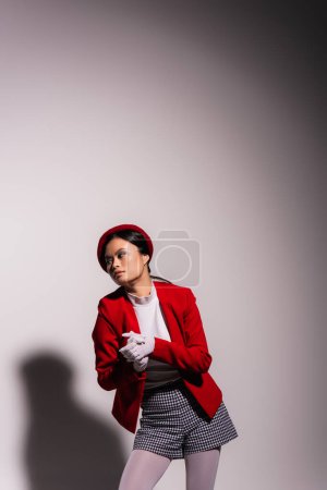 Young asian model in beret and jacket looking away on grey background 