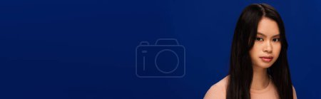 Young asian model with perfect skin standing isolated on navy blue, banner 