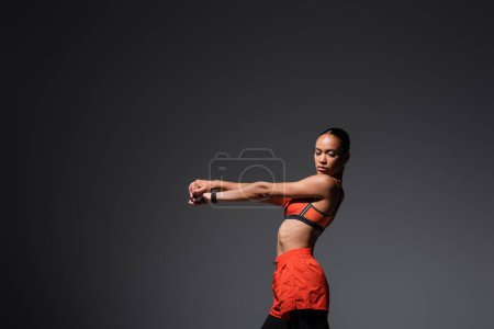 Foto de Brunette african american woman in sports bra working out with outstretched hands isolated on grey - Imagen libre de derechos