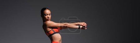 Photo for Brunette african american woman in sports bra working out with outstretched hands isolated on grey, banner - Royalty Free Image