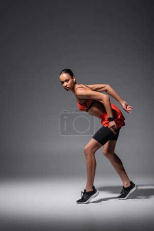 full length of young african american woman in sneakers posing while training on grey 