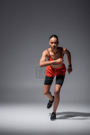 Foto de Full length of young african american sportswoman in sneakers running on grey - Imagen libre de derechos