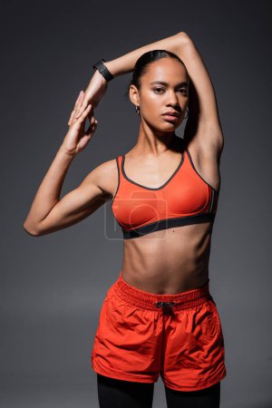 Foto de Young african american sportswoman in red sports bra posing while working out on grey - Imagen libre de derechos