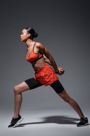 full length of brunette african american woman in sportswear and sneakers exercising on grey 