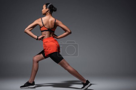 Téléchargez les photos : Full length of young african american woman in sportswear and sneakers exercising with hands on hips on grey - en image libre de droit