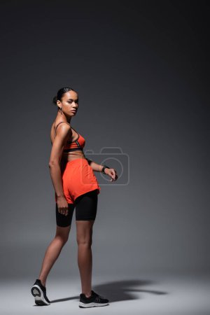Foto de Full length of young african american woman in sportswear and sneakers standing on grey - Imagen libre de derechos