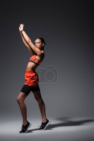 Photo for Full length of tattooed african american sportswoman in sneakers standing with raised arms on grey - Royalty Free Image