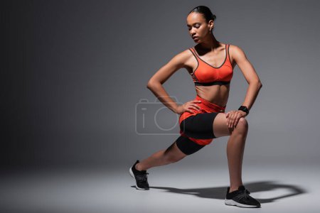 Photo for Full length of young african american woman in sportswear and sneakers exercising with hand on hip on grey - Royalty Free Image