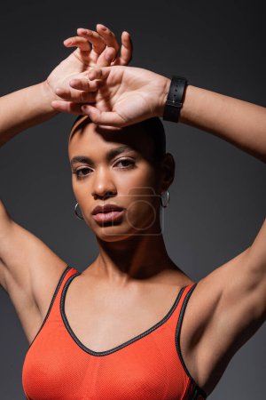 Téléchargez les photos : Young african american woman with fitness tracker posing with raised hands isolated on grey - en image libre de droit