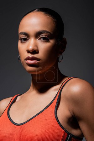 portrait of young african american woman in sports bra looking at camera isolated on grey 