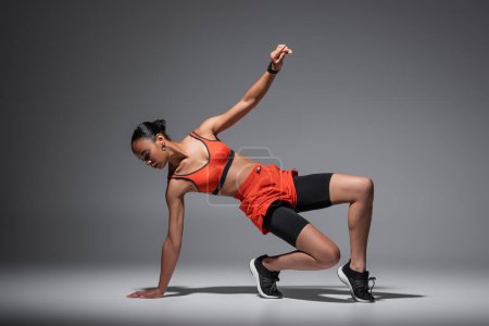 full length of strong and sportive african american woman working out on grey background 