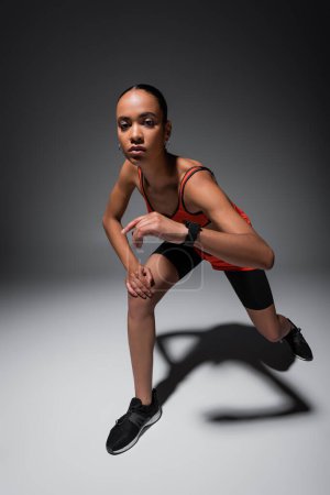 Foto de Full length of brunette african american woman in sportive shorts exercising on grey - Imagen libre de derechos