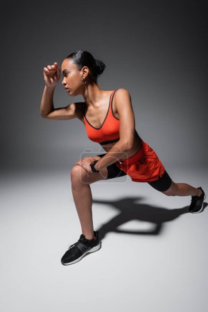 Foto de Tattooed african american woman in sports bra and shorts exercising on grey - Imagen libre de derechos