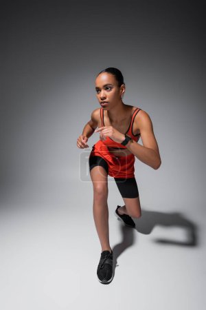 full length of young african american woman in sports bra and shorts working out on grey 