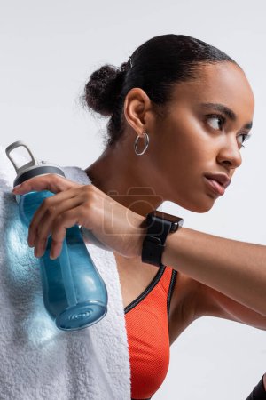young african american woman in sports bra holding sports bottle with water isolated on grey 