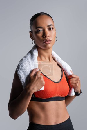 Téléchargez les photos : Young african american sportswoman in red sports bra standing with towel isolated on grey - en image libre de droit