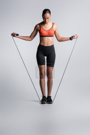 Foto de Full length of sportive african american woman standing with skipping rope on grey - Imagen libre de derechos