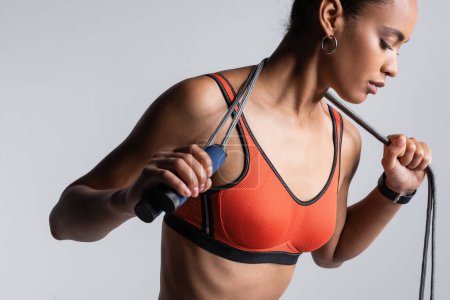 Foto de Young african american sportswoman in red sports bra holding skipping rope isolated on grey - Imagen libre de derechos