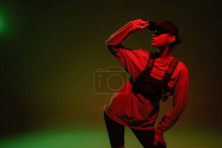 young african american woman in sweatshirt adjusting baseball cap while standing on green with red light 