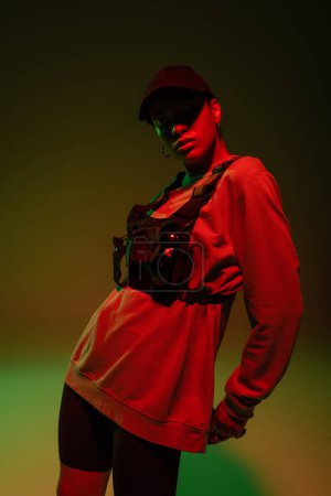african american woman in baseball cap and sweatshirt standing on green with red light 