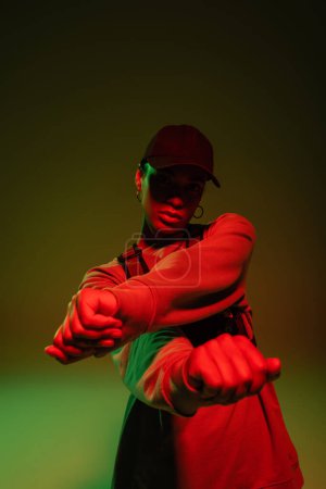 african american woman in sweatshirt and baseball cap posing on green with red light 