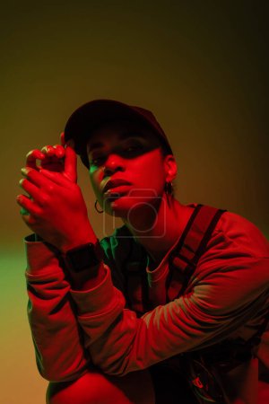 african american woman in baseball cap looking at camera on green with red light 