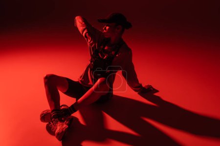 Photo for High angle view of stylish african american woman in baseball cap and sweatshirt sitting on red - Royalty Free Image