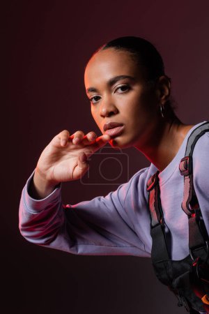 young african american woman in sweatshirt looking at camera on dark purple 
