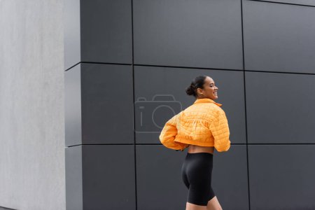 Photo for Cheerful african american sportswoman in bike shorts and yellow puffer jacket exercising outside - Royalty Free Image