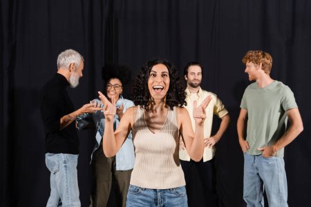 excited multiracial actress rehearsing near young actors and mature screenwriter in theater