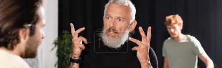 Photo for Bearded middle aged art director gesturing near blurred actors in acting skills school, banner - Royalty Free Image