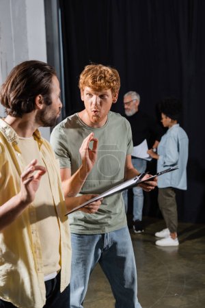 young actors with clipboards grimacing and showing okay signs during rehearsal in acting school