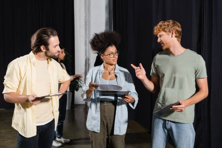 redhead man pointing with finger while talking to interracial students with screenplays in theater