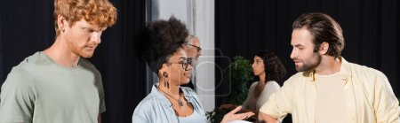 happy african american woman talking to bearded actor near interracial students in theater studio, banner