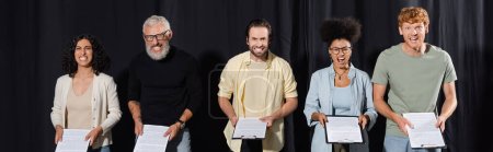 Foto de Bearded art director with interracial students grimacing while holding screenplays, banner - Imagen libre de derechos