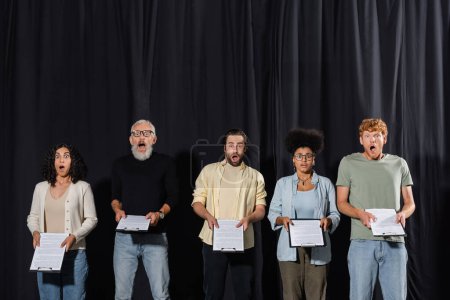 amazed multicultural actors with bearded art director holding clipboards during rehearsal in acting school