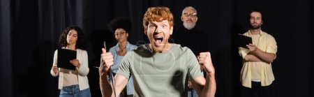 Foto de Excited redhead man shouting and showing like gesture near producer and multiethnic actors on blurred background, banner - Imagen libre de derechos