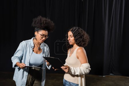Foto de Young interracial actresses looking at clipboards with scenarios in theater - Imagen libre de derechos