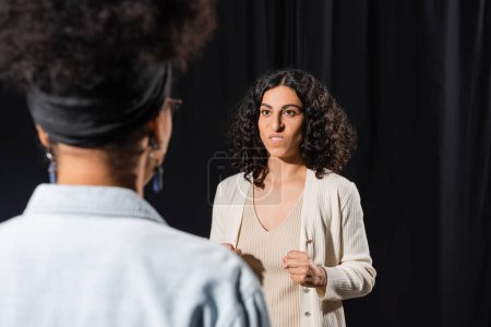 multiracial actress grimacing while rehearsing near blurred african american actress in theater