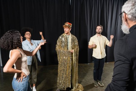 interracial actors posing near man in king costume near art director on blurred foreground