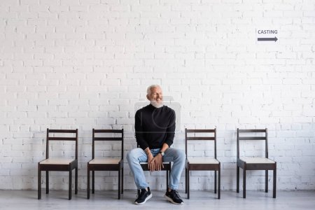 bearded man smiling with closed eyes while sitting on chair and waiting for casting