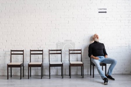 Foto de Full length of mature man sleeping on chair while waiting for casting on chair near white wall - Imagen libre de derechos