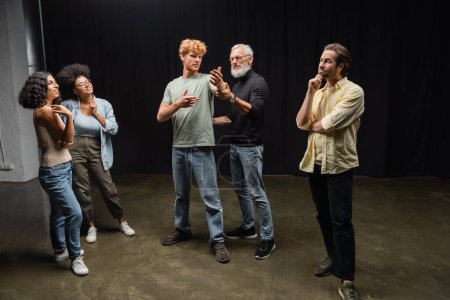 mature art director assisting redhead man during rehearsing near emotional interracial actors. Translation of tattoo: kanji, danger