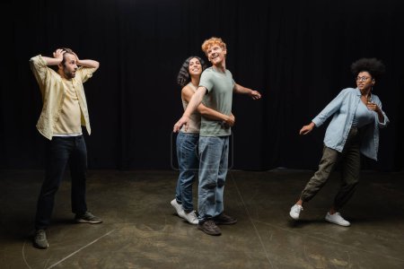 full length of emotional interracial students of acting skills school rehearsing in theater